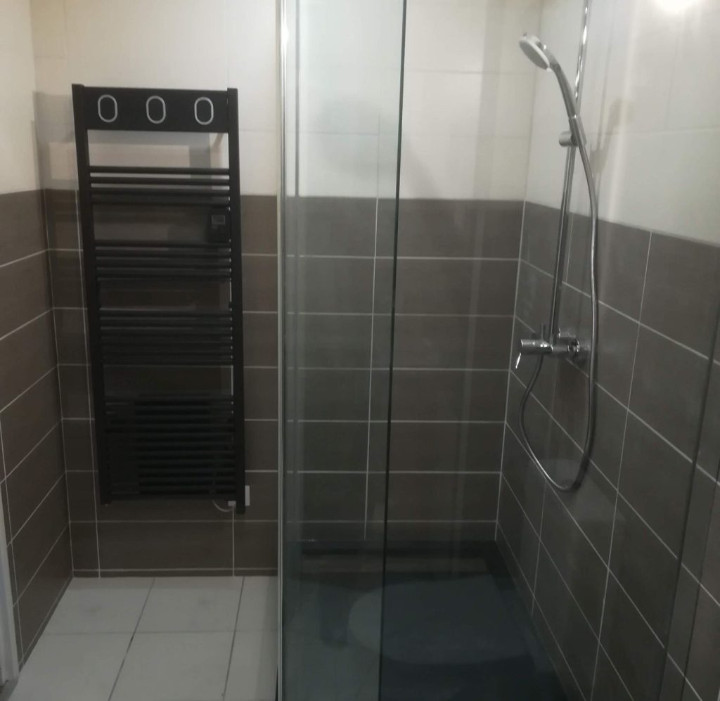 Salle de douche : Cabine de douche carrelée en gris avec porte vitrée.